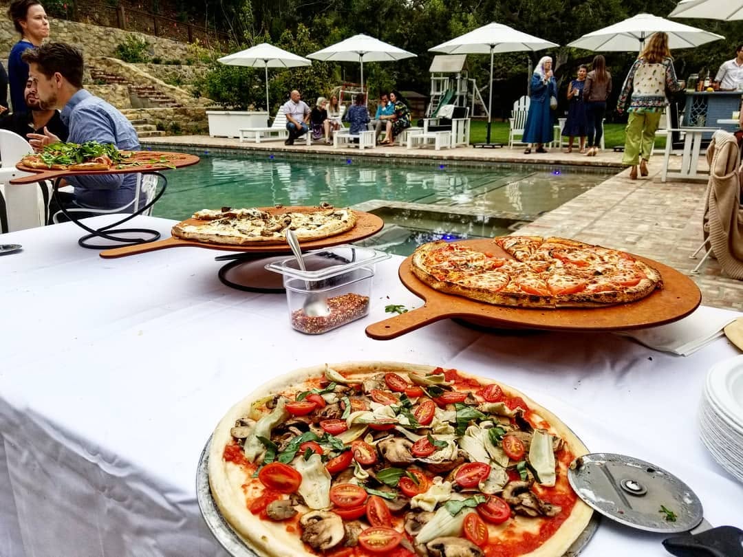 Fresh-baked pizzas on wooden peels beside a poolside table at a private Orange County backyard party